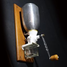 an old fashioned coffee grinder mounted on a wooden wall with a metal cup attached to it