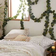 an unmade bed with white sheets and pillows next to a window filled with greenery