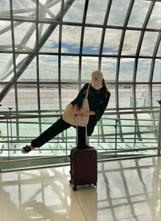 a woman sitting on top of a piece of luggage in front of a glass wall