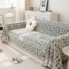 a living room with a couch covered in a white and black patterned cover next to a window