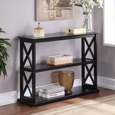 a black shelf with books and vases on it in front of a painting hanging on the wall