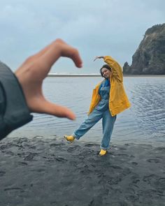 a woman is dancing on the beach with her hand in front of her and another person reaching out