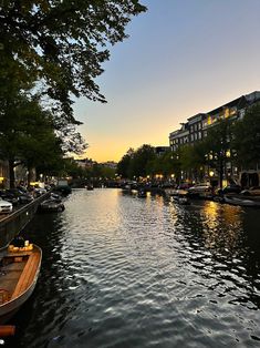 boats are lined up along the side of a river at sunset or dawn in an urban area