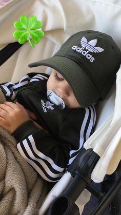 a baby in a stroller wearing a adidas hat