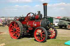 an old fashioned steam engine on display in a field with other antique vehicles and people