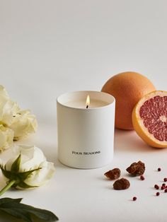 a grapefruit candle next to some flowers and an orange on a white surface