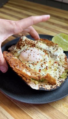 a person is pointing at an egg in toast on a plate with a lime wedge