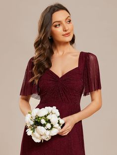 a woman in a red dress holding a bouquet of white flowers and posing for the camera