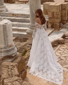 a woman in a white wedding dress is standing on some stone steps and looking off into the distance