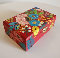 a colorful painted box sitting on top of a white table next to a vase with flowers