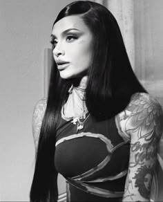 a woman with long black hair and tattoos on her arm, wearing a bodysuit