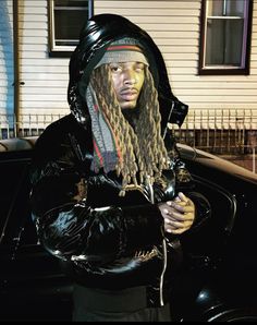 a man with dreadlocks and a hoodie sitting in front of a car