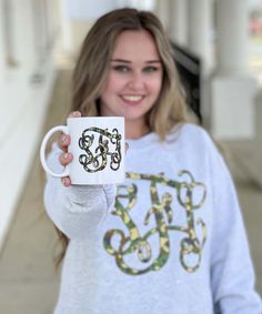 a woman holding up a coffee mug with the letter e on it in front of her