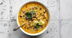 a white bowl filled with soup and topped with cilantro, parsley and lime