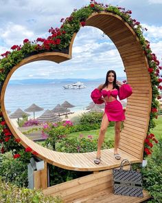 a woman in a pink dress standing on a wooden heart shaped bench with flowers around her