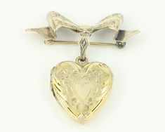 Vintage 10K GF Heart Locket Bow Brooch. This romantic 10K gold filled piece features an engraved and embossed heart shaped locket suspended from an engraved bow pin finished with roll over safety. The locket holds two photos and has a side hinge. Both hinge and clasp work nicely. It has both photo frames, one celluloid cover, and both gold foil paper liners. Good vintage condition with very minor surface wear and patina and no damage noted.  ERA: Mid-Century, 1940s    METAL/MATERIALS: 1/20 10K G Antique Heart Brooch For Wedding, Antique Heart-shaped Wedding Brooch, Vintage Engraved Brooches For Anniversary, Vintage Heart-shaped Brooch Jewelry, Vintage Heart Shaped Brooch Jewelry, Antique Heart-shaped Brooch For Gift, Vintage Brooch For Valentine's Day Formal, Vintage Brooch Jewelry For Valentine's Day, Vintage Heart Shaped Brooch