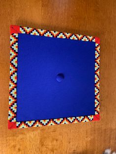 a wooden table topped with a blue square covered in beadwork and a button