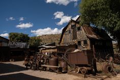 an old wooden building sitting in the middle of a dirt lot next to a tree