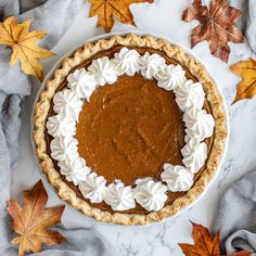 a pumpkin pie with whipped cream on top and autumn leaves around the edges, sitting on a marble surface