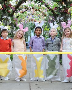 four children in bunny ears are standing behind a yellow and white fence with easter bunnies on it