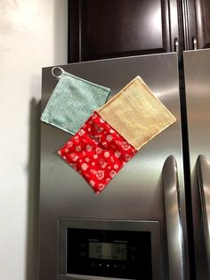 two kitchen towels hanging on the side of a stainless steel refrigerator with magnets attached to it