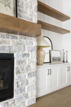 a stone fireplace in a living room next to white cupboards and a painting on the wall