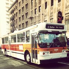 an orange and white bus is driving down the street in front of some tall buildings