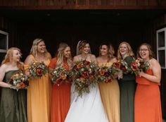 a group of women standing next to each other holding bouquets in front of a barn