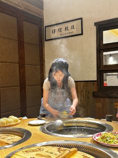 a woman cooking food on top of a wooden table next to other plates and bowls