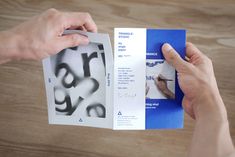 two hands holding an open brochure on top of a wooden table