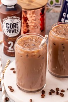 two glasses filled with iced coffee sitting on top of a white plate next to chocolate chips