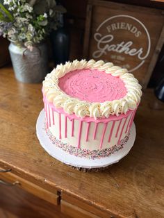 a cake with pink frosting and sprinkles sitting on top of a wooden table