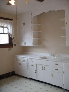 an empty kitchen with white cupboards and drawers in it's center area, next to a window