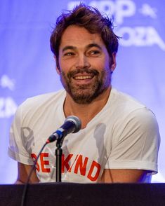 a smiling man sitting in front of a microphone