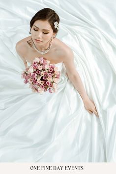 a woman in a wedding dress laying on a bed holding a bouquet of pink flowers