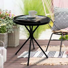 a small table and chair on a deck with potted plants in the back ground