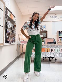 a woman in green pants and white shirt posing for the camera with her hands up