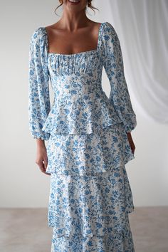 a woman wearing a blue and white floral print dress with puffy sleeves, smiling at the camera