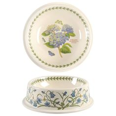 a white bowl with blue flowers and green leaves on the bottom, sitting next to a plate