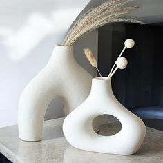 two white vases sitting on top of a counter next to each other with dried grass in them