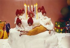 a group of people laying on top of a bed covered in pillows and hats with candles behind them