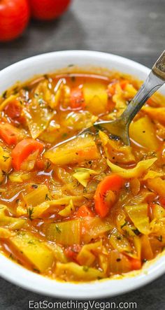 a white bowl filled with vegetable soup next to tomatoes