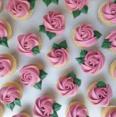 cupcakes with pink frosting and green leaves on white tablecloth, top view