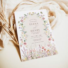 the wedding card is laying on top of some white fabric and it's floral design