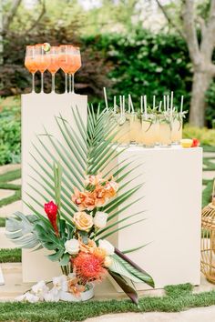 an arrangement of flowers and drinks on display in the grass at a wedding reception with palm leaves