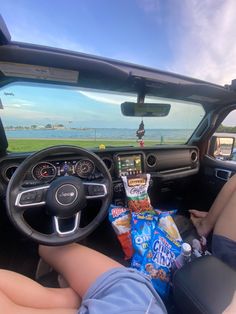 a person sitting in the driver's seat of a car with snacks and chips