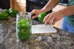 a person cutting green peppers in half on a kitchen counter top with a glass jar full of them