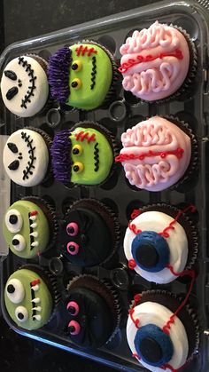 cupcakes decorated to look like halloween characters are displayed in a plastic container on a table