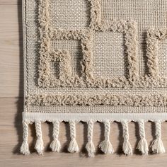 an area rug with fringes and squares on top of wooden flooring, close up