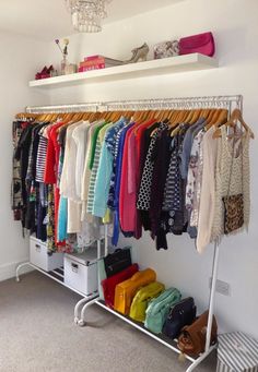 an organized closet with clothes and handbags hanging on the rack, in front of a white wall